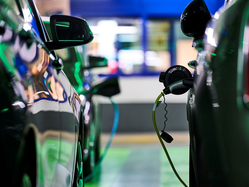 Zwei Autos stehen dicht nebeneinander. Beim rechten Auto ist der Stecker zum E-Laden angeschlossen.